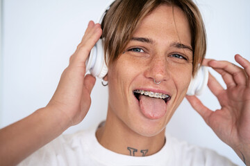 Playful short haired blonde woman with facial piercing and dental braces on teeth listening music...