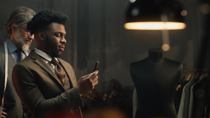 African American businessman in luxury designer tailoring studio. Man takes picture of suit or...