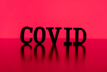 COVID spelled out with letter tiles in silhouette backlit by blood red illuminated screen.