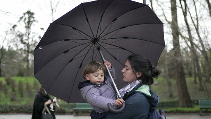 Baby toddler and mother holding umbrella outside at park during rainy drizzle day