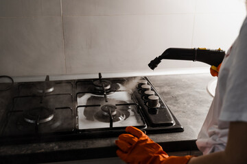 Worker of cleaning service is steaming on cooker using steam generator. Steam cleaning of cooker in...
