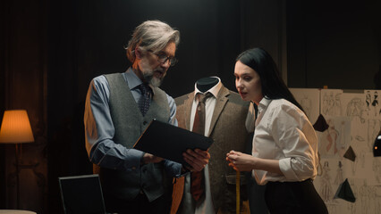 Male and female tailors work on business or wedding suit. Man draws sketch on tablet computer. Mannequin in tailored suit in designer atelier or tailoring studio. Fashion and hand craft concept.