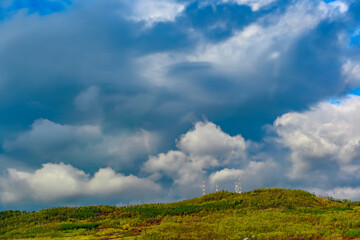 Towers with telecommunication antennas located on top of the hills covered in colorful trees, autumn dramatic landscape with stormy clouds rushing over the dark blue sky. Natural vibrant Earth scenery
