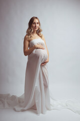 Fototapeta na wymiar Elegant pregnant young woman standing wearing light fabric. Pregnancy, fantasy and fairy tale concept.