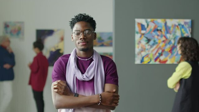 Waist up portrait shot of young black man posing for camera with arms crossed while standing in exhibition hall of art gallery
