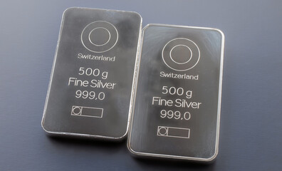 Two minted silver bars weighing 500 grams each. On a grey blue background.