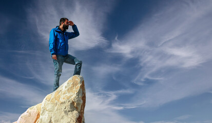 The hiker on top of the mountain. A young, athletic man stands on a high rock. Sporty man standing on stone against valley, active life concept