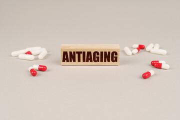 On a gray surface are tablets, capsules and a wooden plate with the inscription - ANTIAGING