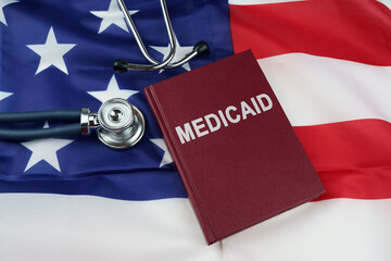 On the US flag lies a stethoscope and a book with the inscription - Medicaid