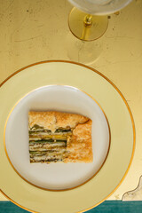 single serving, rectangular slice of an asparagus gruyere galette on golden yellow plate with yellow stemmed glassware