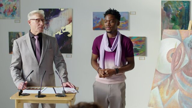 Young African American artist presenting painting to audience from stage while selling it on art auction