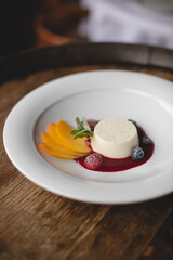 Restaurant serving dessert. Panna cotta on a white plate with jam and fresh fruit