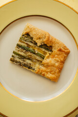 single serving, rectangular slice of an asparagus gruyere galette on golden yellow plate