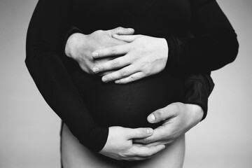 black and white photo of unrecognizable body of pregnant woman in black bodysuit and hands of parents intertwined on stomach