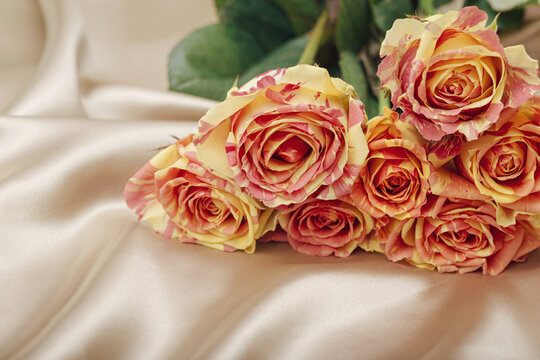 Bouquet of colorful rose flowers on beige satin cloth closeup. Love and romance theme. Valentine day concept. Beautiful floral background