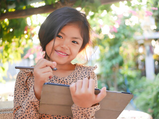 Asian girl is happy and enjoys using a tablet outdoors with a stylus in her hand: for e-learning,...