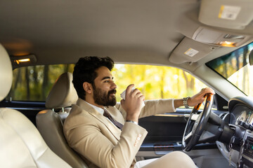 Smiling arab businessman driving a car while drinking coffee