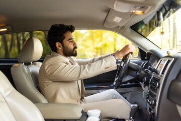 Happy middle eastern young businessman driving new auto looking at road and smiling