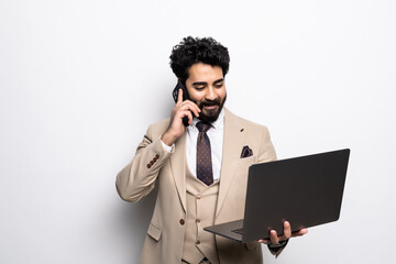 Portrait of a arab businessman holding laptop computer while standing and talking on mobile phone isolated over white background