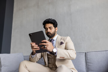 Portrait of a handsome young businessman sitting on a modern couch, holding a digital tablet