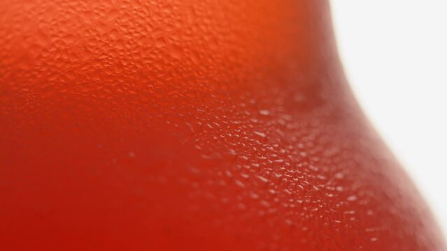 Macro close-up shot focusing on the texture of condensation droplets on a cold amber glass beer bottle. The chilled surface reflects warm light, creating an appetizing, refreshing look for ads