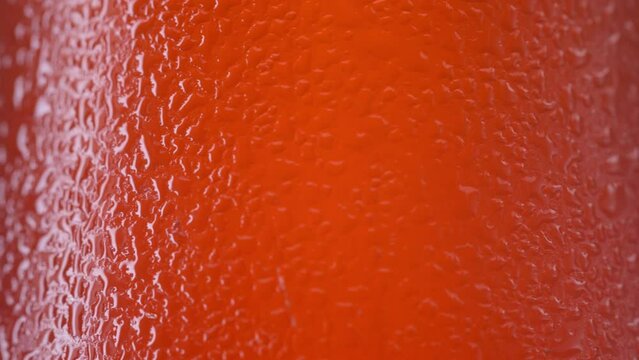 Macro close-up of condensation and moisture beads on the surface of an ice cold plastic bottle filled with bright orange soda. The refreshing droplets cling to the chilled container, indicating a cold