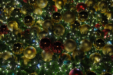 Red, golden, shiny Christmas balls on a green Christmas tree with a white flashing garland