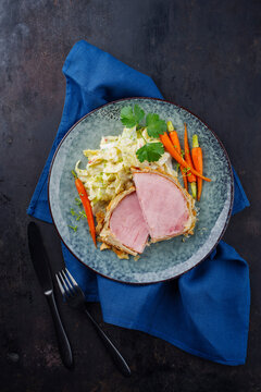 Gebackenes Kasseler Schweinesteak im Teigmantel mit Wirsing Kohl und Baby Karotten serviert als Draufsicht auf einem Design Teller mit Textfreiraum