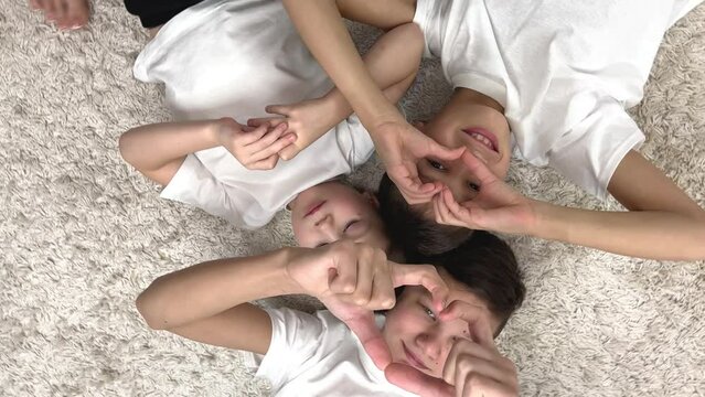 three boys brothers lie on the floor and show a heart with hands they are in white t-shirts smiling they lie head to head with star snowflake white carpet concept of friendship happiness family joy