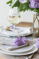 Beautiful table decor for a wedding dinner with a spring blooming lilac flowers. Celebration of a special event. Fancy white plates, wineglasses. Countryside style