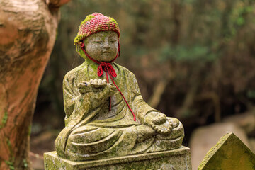 Stone statue of child sitting cross-legged wearing a knit cap at Japanese shrine