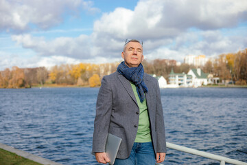 Old businessman in stylish clothes enjoying with closed eyes natural beauty. Man walk outdoors near water pond. 