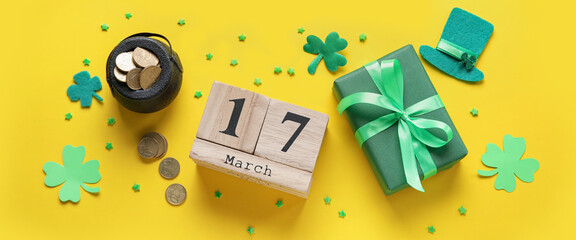 Leprechaun's pot with golden coins, gift and calendar with date of St. Patrick's Day on yellow background