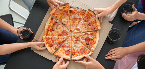 Young people taking slices of hot tasty pizza from cardboard box, top view