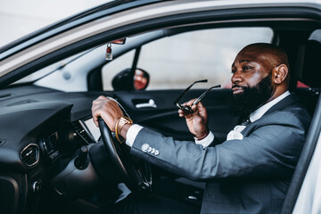 A view of a sophisticated black male, in selective focus, with one hand on the steering wheel and...
