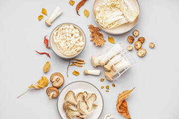 Composition with different fresh mushrooms and autumn leaves on light background