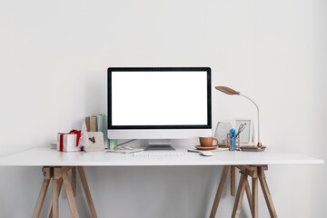 Workplace with computer, cup and Christmas gift near light wall