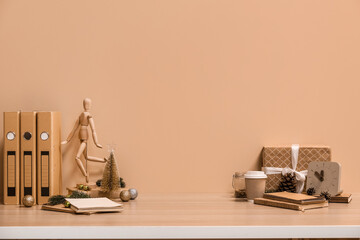 Christmas decor with coffee cup, folders and gift on table near beige wall