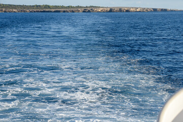 View from rear of a boat sailing away from an island