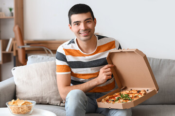 Young man with box of tasty pizza sitting on sofa at home