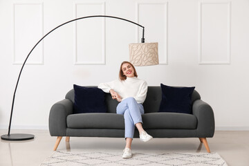 Young woman sitting on black couch near light wall