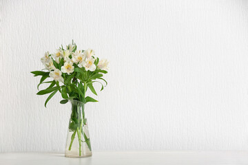 Vase with beautiful alstroemeria flowers on table near light wall