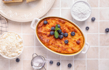 Delicious cheese pie with fresh blueberry in baking form and ingredients on white tile table