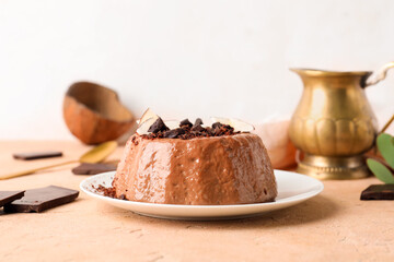 Plate with delicious pudding, coconut slices, chocolate and jug on beige table