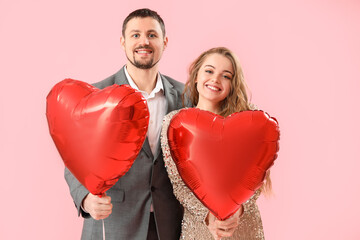 Fototapeta na wymiar Happy young couple with heart-shaped balloons on pink background. Valentine's Day celebration