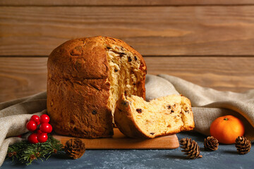 Board with Panettone, fir cones and mandarin on table near wooden wall