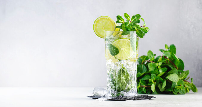 Mojito classic summer alcoholic cocktail with lime, white rum, soda, cane sugar, mint, and ice in highball glass on gray background. Copy space banner