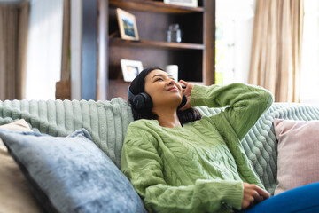 Obraz premium Image of happy biracial woman in headphones, relaxing on sofa with eyes closed at home, copy space