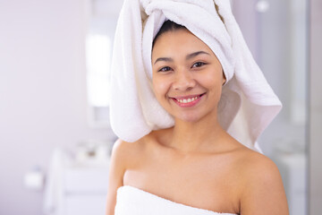 Portrait of happy biracial woman wearing towel smiling in bathroom, with copy space