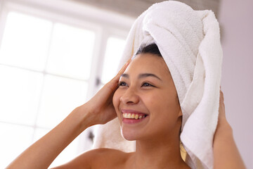 Happy biracial woman wearing towel on head smiling in bathroom, with copy space